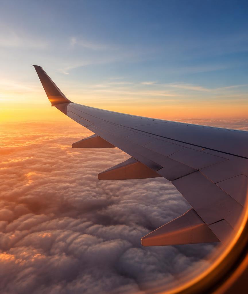 View of an aircraft wing above clouds at sunset from a passenger window